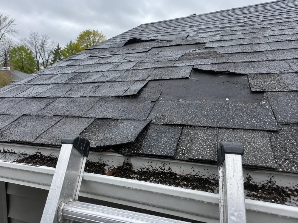 Wind-damaged asphalt roof with torn and missing shingles